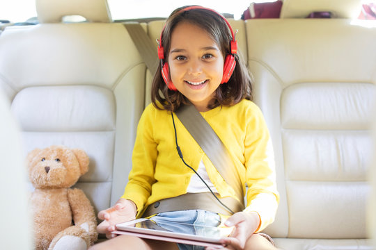 Portrait smiling, confident girl watching movie headphones digital tablet in back seat of car