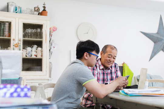 Son helping senior father paying bills at laptop
