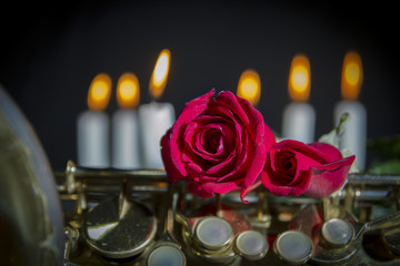 two red rose on a saxophone close up and flaming candles in  black background , valentines day and...