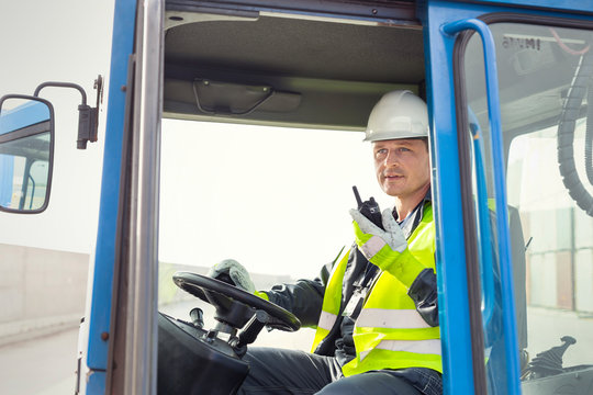 Dock worker using walkie-talkie and operating crane at shipyard