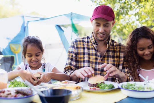 Father and daughters enjoying hamburger lunch at campsite