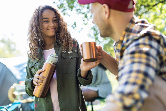 Daughter pouring coffee from insulated drink container fro father at campsite