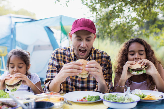 Father and daughters eating barbecue hamburgers at campsite