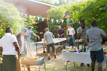 Male friends playing ping pong, enjoying backyard barbecue