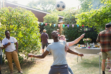Male friends playing soccer, enjoying backyard summer barbecue