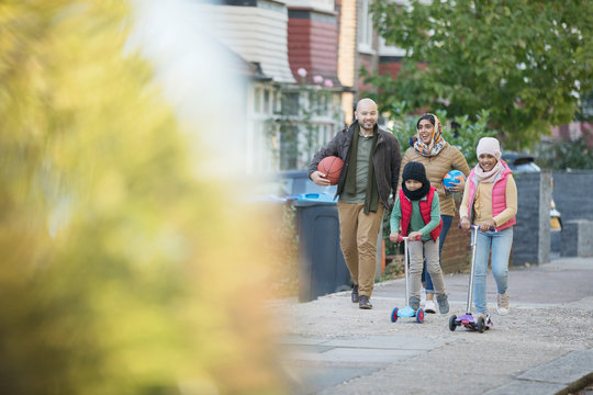 Muslim family walking and riding scooters on neighborhood sidewalk