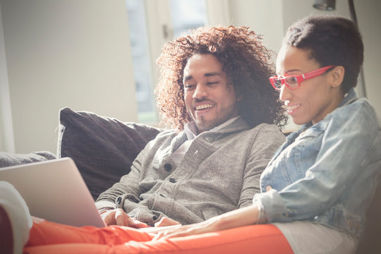Couple relaxing, using laptop on sofa
