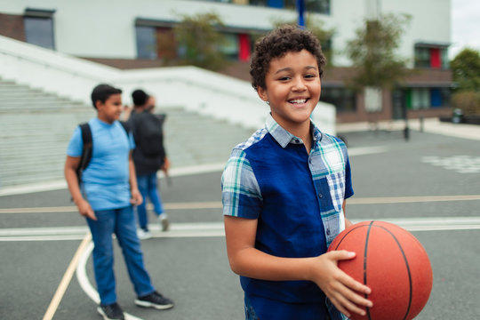 Portrait smiling, confident tween boy playing basketball in schoolyard