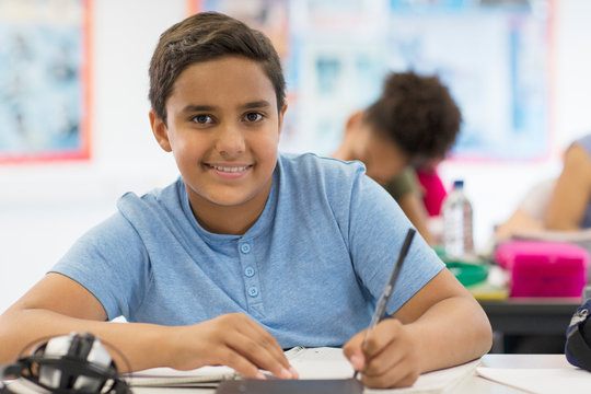 Portrait confident junior high school boy student doing homework in classroom
