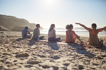 Group sitting on yoga mats on sunny beach during yoga retreat