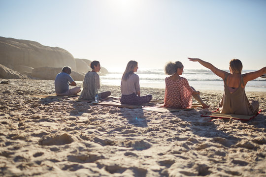 Group sitting on yoga mats on sunny beach during yoga retreat