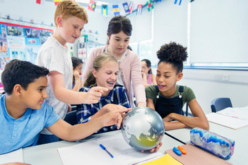 Curious junior high school students looking at globe in classroom