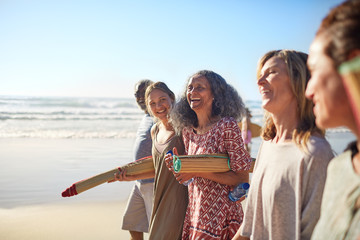 Happy friends with yoga mats on sunny beach during yoga retreat