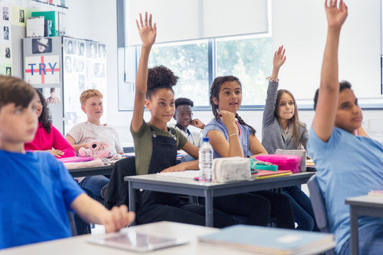 Junior high school students with hands raised in classroom - Powered by Adobe