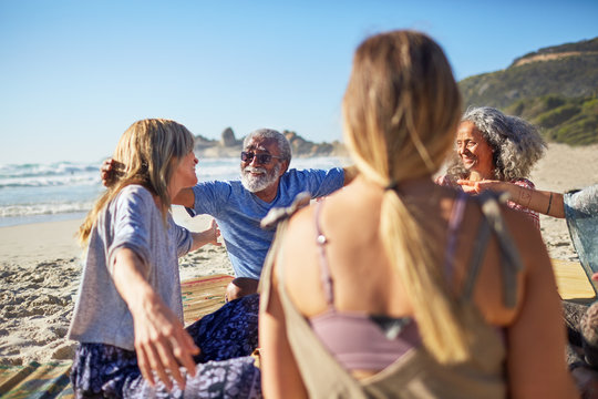 Friends hugging in circle on sunny beach during yoga retreat
