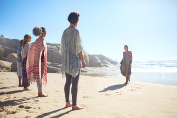 Woman leading yoga class on sunny beach during yoga retreat