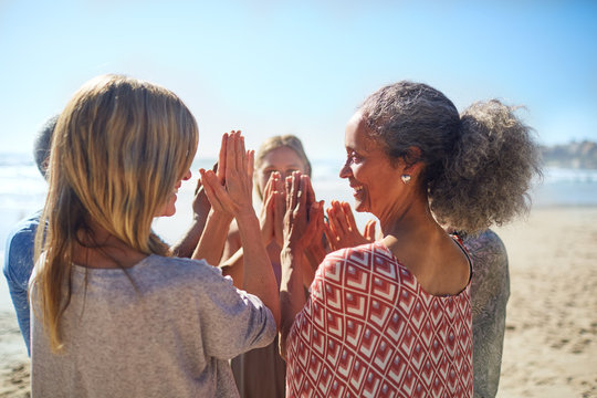 Women friends hands clasped in circle on sunny beach during yoga retreat