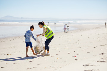 Mother and son volunteers cleaning up litter on sunny, sandy beach