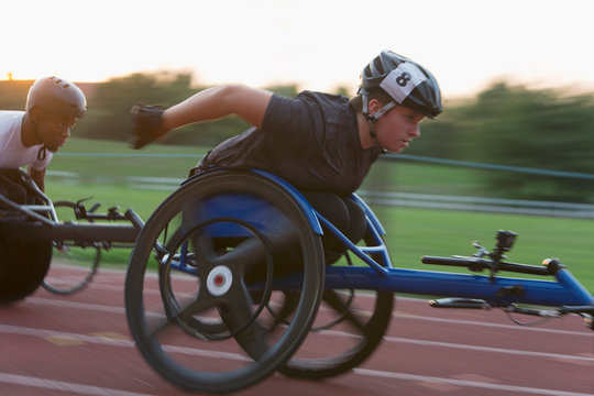 Determined young female paraplegic athlete speeding along sports track in wheelchair race