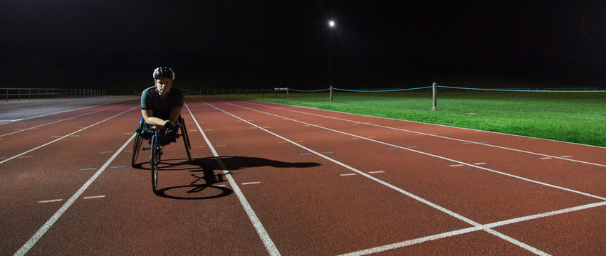 Portrait confident, determined young female paraplegic athlete training for wheelchair race on sports track at night