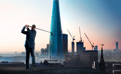 Businessman swinging golf club on city highrise rooftop