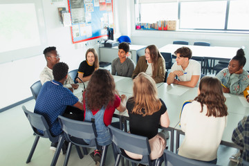 High school students talking in debate class at table in classroom