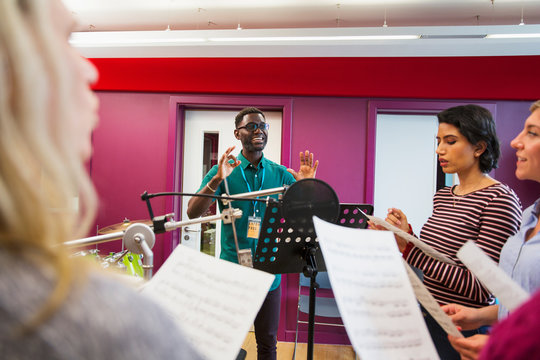 Male conductor leading womens choir sheet music singing in music recording studio