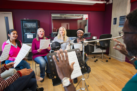 Male conductor leading womens choir sheet music singing in music recording studio
