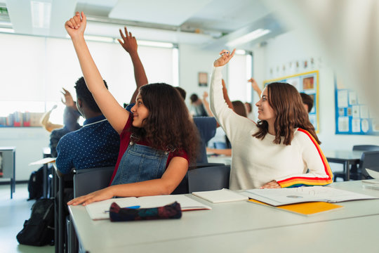 High School Girl Students With Hands Raised During Lesson In Classroom