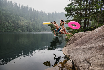 Playful young couple inflatable rings jumping into remote lake, Squamish, British Columbia, Canada