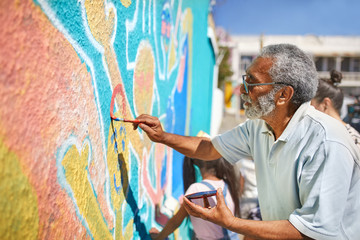 Senior male volunteer painting vibrant mural on sunny wall