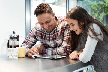 Smiling father and daughter using digital tablet at kitchen counter