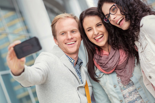 Playful young friends taking selfie with camera phone