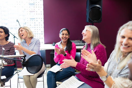 Happy womens choir sheet music singing clapping in music recording studio