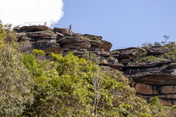 Naklejka premium People as small silhoutted specks on the huge plateau with sticking out rock formations in the Andorinhas [swallows] park in Ouro Preto seen from a lower viewpoint against a blue sky with cloud