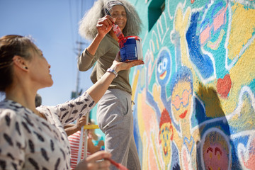 Female volunteers painting vibrant community mural on sunny urban wall