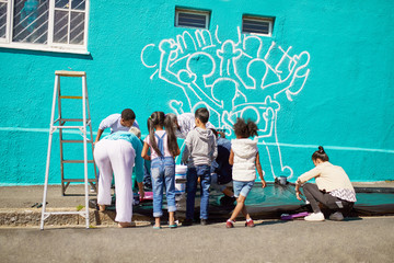 Kid volunteers painting community mural on sunny wall