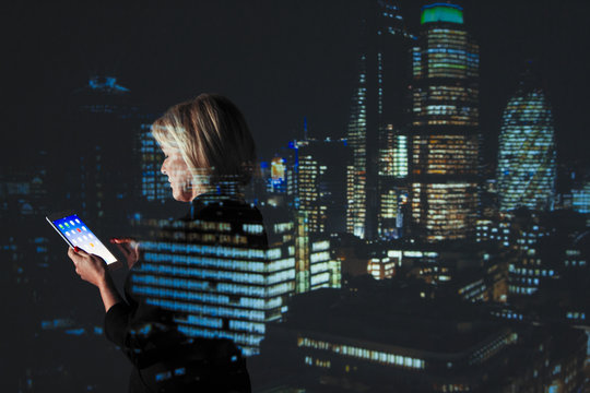 Double exposure businesswoman using digital tablet against highrise lights at night