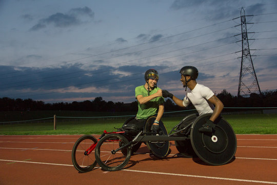 Paraplegic athletes fist bumping on sports track, training for wheelchair race at night