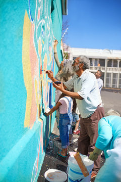 Community volunteers painting vibrant mural on sunny urban wall