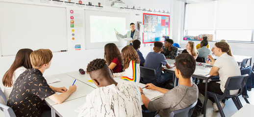 High school students watching teacher at projection screen during lesson in classroom