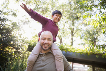 Portrait playful father carrying son on shoulders in park
