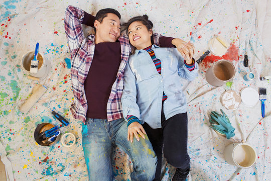 Happy couple relaxing, taking a break from painting, laying on dropcloth among paint cans