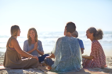 Happy friends talking in circle on sunny beach during yoga retreat