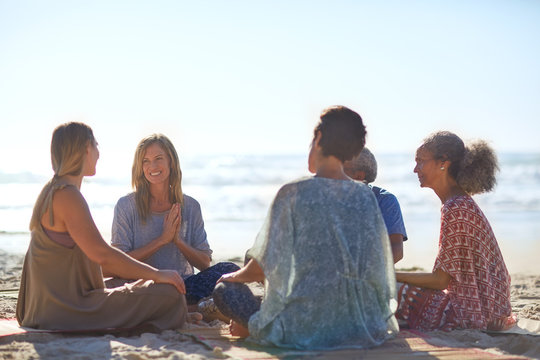 Happy friends talking in circle on sunny beach during yoga retreat