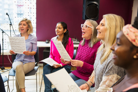 Womens choir with sheet music singing in music recording studio