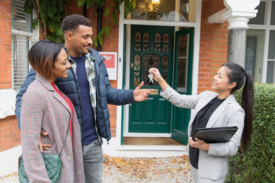 Real estate agent giving house keys to couple outside new house