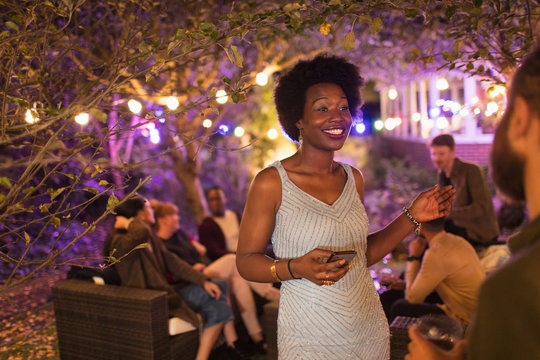 Smiling woman with smart phone talking to friend at garden party