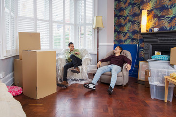 Men taking a break from moving house, relaxing and laughing in armchairs