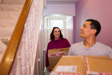 Happy couple moving into new house, carrying cardboard boxes in corridor